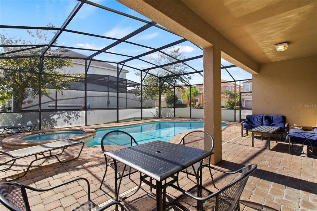 A covered patio features a pool, a hot tub, and outdoor furniture on a brick deck — 4414 SHIVA LOOP, KISSIMMEE, FL