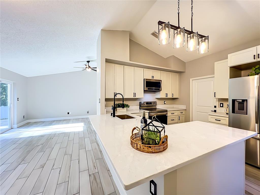 A modern kitchen features white cabinetry, quartz countertops, stainless steel appliances, and wood-look tile flooring — 5915 GROVELINE DRIVE, ORLANDO, FL