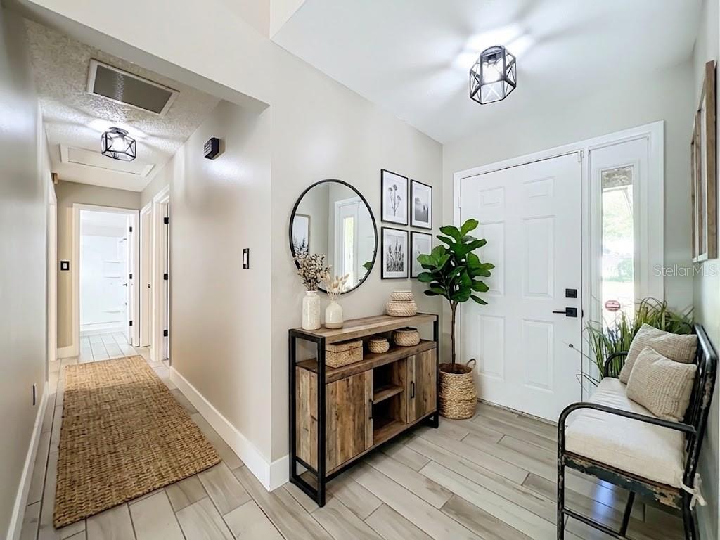A bright entryway features wood-look tile flooring, a rustic console table, and a metal bench — 5915 GROVELINE DRIVE, ORLANDO, FL