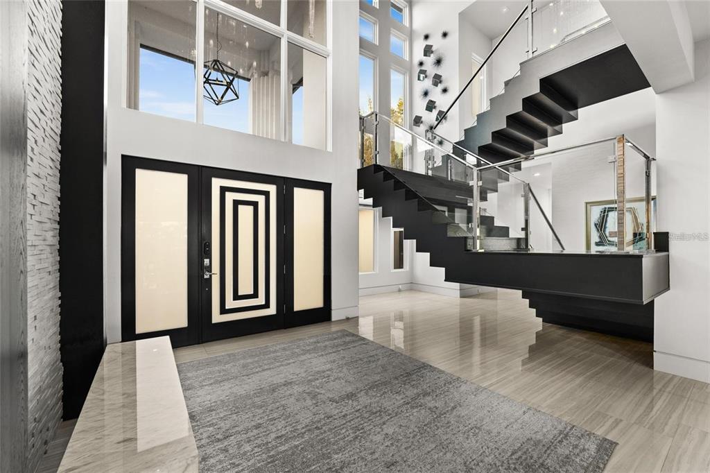 A modern foyer features a floating black staircase, glass railings, and a large front door — 12264 MONTALCINO CIRCLE, WINDERMERE, FL