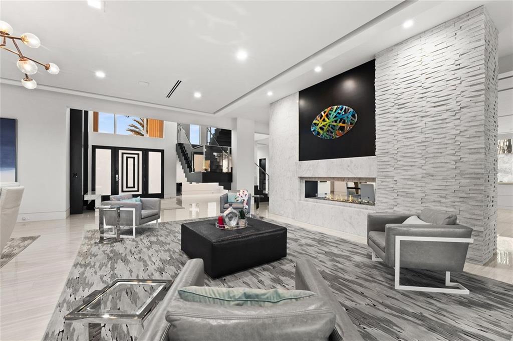 A modern living room features a stone fireplace, gray armchairs, and a large area rug — 12264 MONTALCINO CIRCLE, WINDERMERE, FL