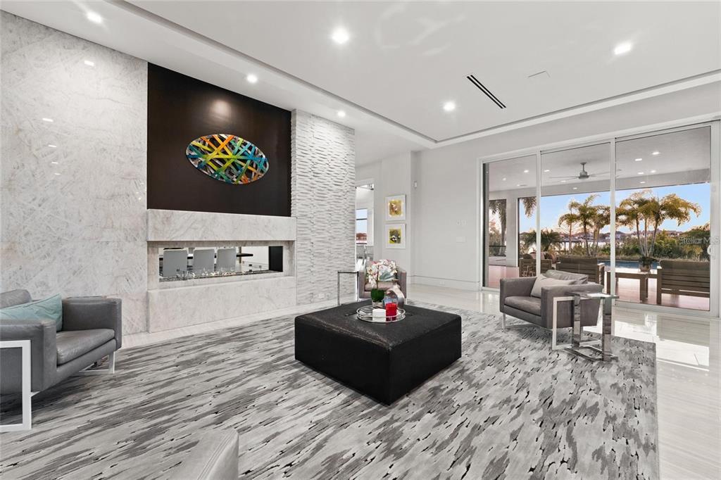 A modern living room features a marble fireplace, a black ottoman, and large glass doors — 12264 MONTALCINO CIRCLE, WINDERMERE, FL