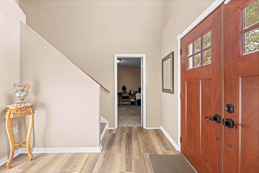 An entryway features wood-look flooring, a wooden front door, and a staircase with a railing — 7319 LAGOON ROAD, SPRING HILL, FL