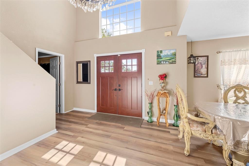 A high-ceilinged entryway features double wood front doors, light wood flooring, and a dining area — 7319 LAGOON ROAD, SPRING HILL, FL