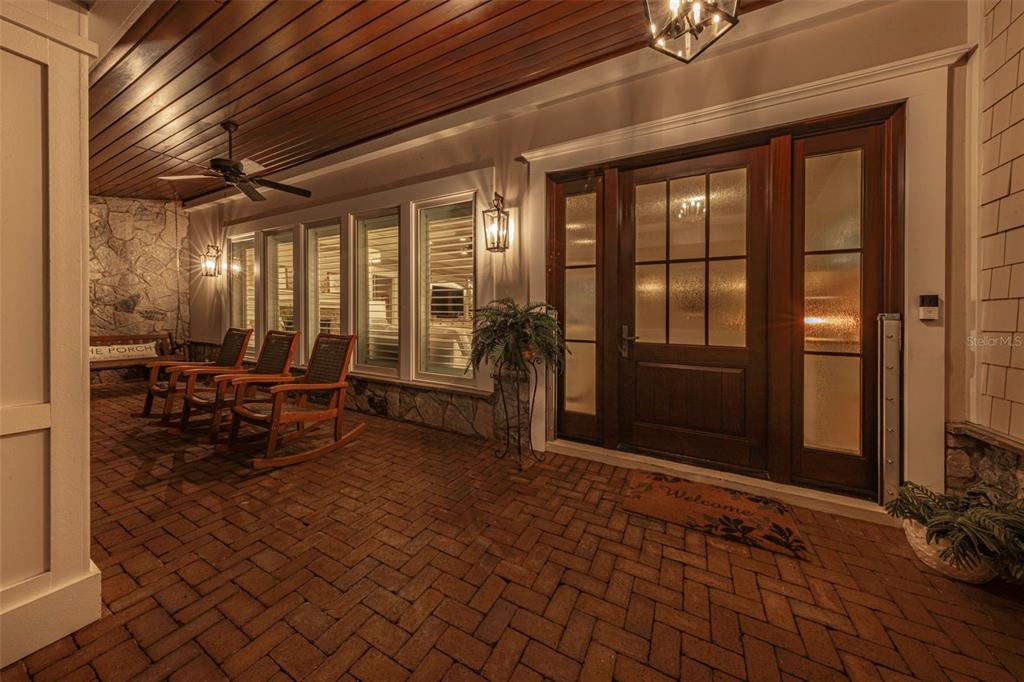 A covered brick porch features rocking chairs, a wooden ceiling, and a large front door — 1744 SANTA BARBARA DRIVE, DUNEDIN, FL