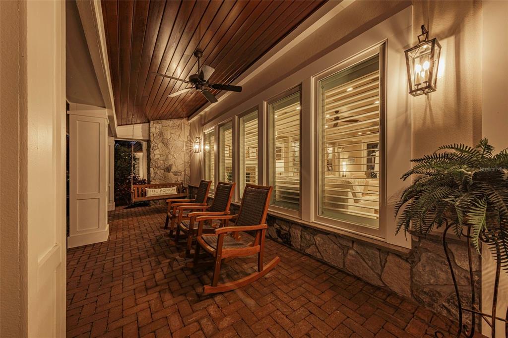 A covered brick porch features rocking chairs, a ceiling fan, and a stone accent wall — 1744 SANTA BARBARA DRIVE, DUNEDIN, FL
