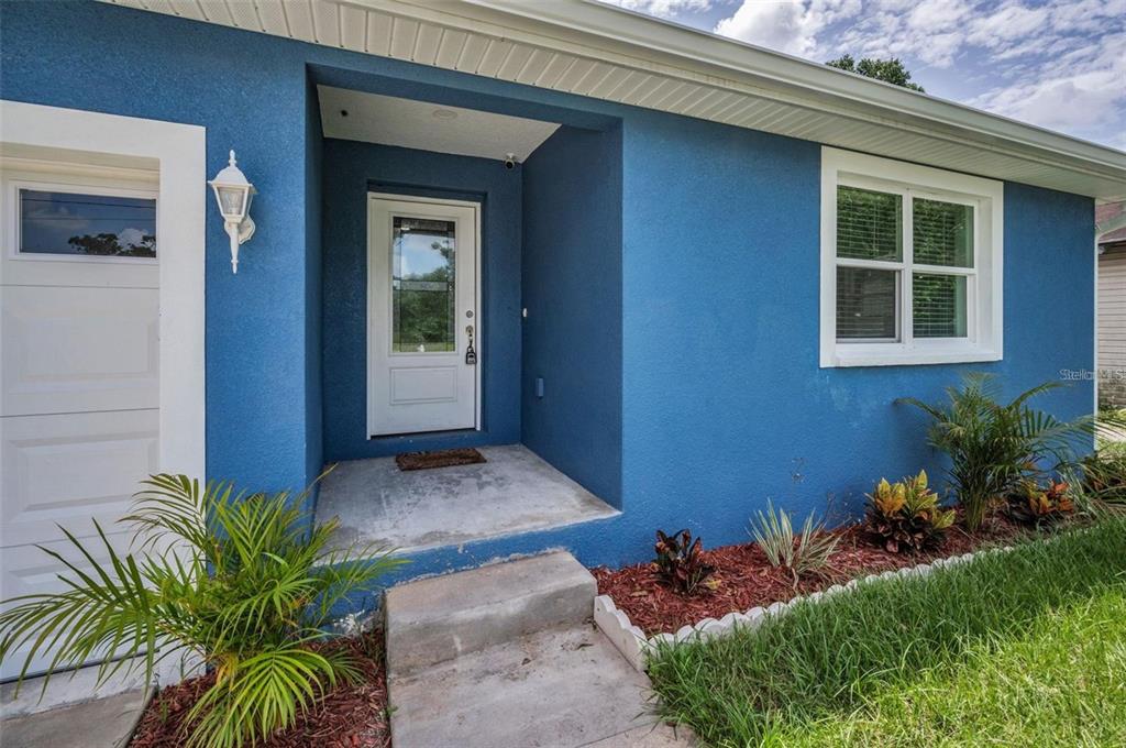 A blue stucco house exterior features a white front door, a window, and landscaping — 2307 N 47TH STREET, TAMPA, FL