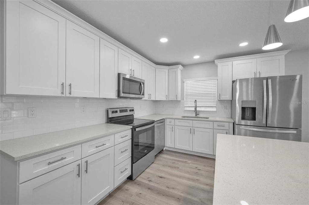A modern kitchen features white shaker cabinets, stainless steel appliances, and light-colored quartz countertops — 2307 N 47TH STREET, TAMPA, FL