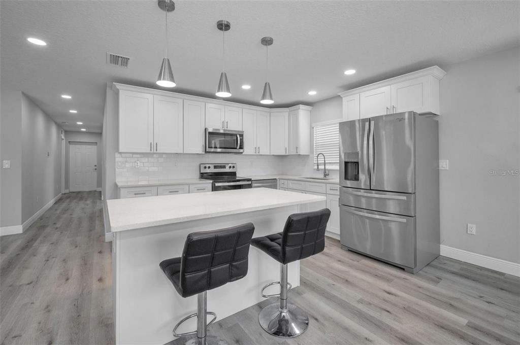 A modern kitchen features white cabinets, stainless steel appliances, a center island, and wood-look flooring — 2307 N 47TH STREET, TAMPA, FL