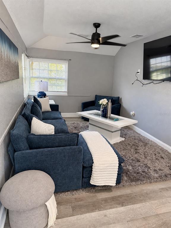 A living room with gray walls, wood-look flooring, a black sofa, and a wall-mounted television — 1340 13TH AVENUE S, ST PETERSBURG, FL