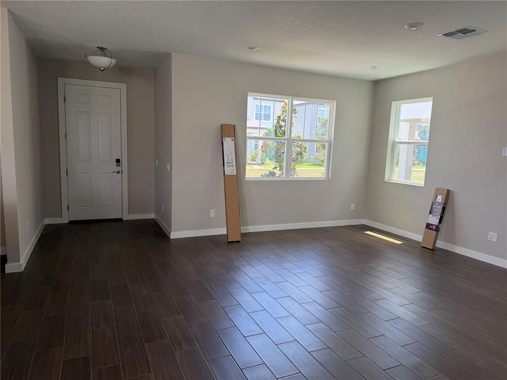 An empty room features dark wood-look tile flooring, light gray walls, and two windows — 17819 TWISTED MANDARIN ALLEY, WINTER GARDEN, FL