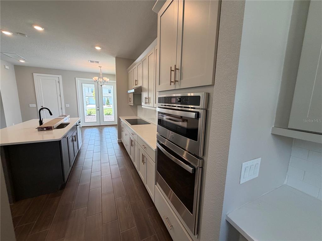 A modern kitchen features light-colored cabinetry, stainless steel wall ovens, and a dark kitchen island — 17819 TWISTED MANDARIN ALLEY, WINTER GARDEN, FL