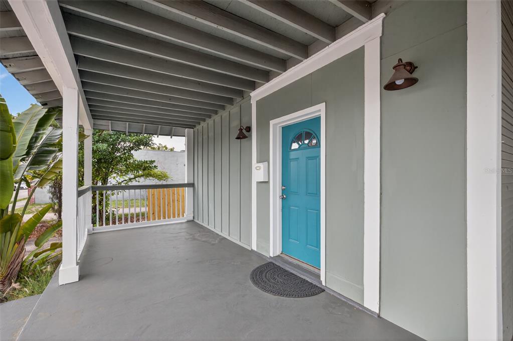 A covered porch features gray painted flooring, board-and-batten siding, and a bright blue front door — 105 W COLUMBUS DRIVE, TAMPA, FL