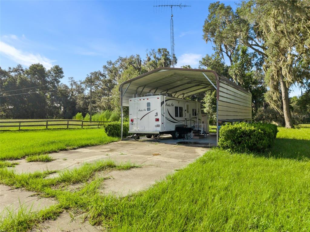 A white travel trailer is parked under a metal carport on a concrete pad outdoors — 390 SE 30TH AVENUE, TRENTON, FL
