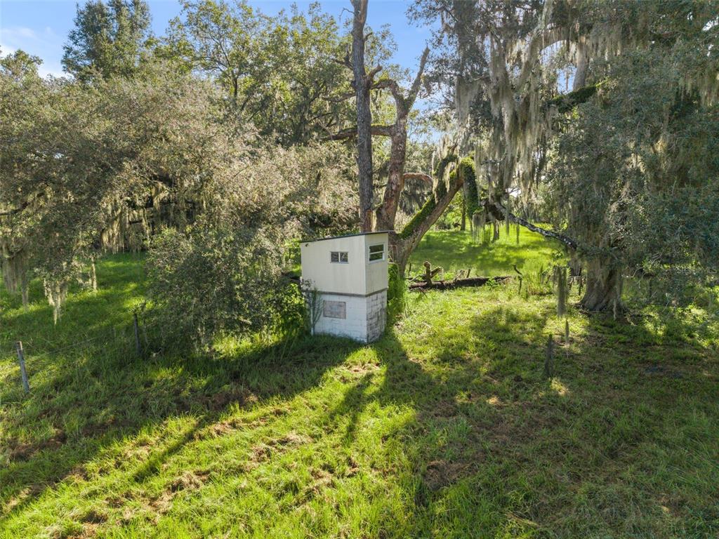 A small, weathered shed with a concrete block base sits in a grassy, tree-filled field — 390 SE 30TH AVENUE, TRENTON, FL