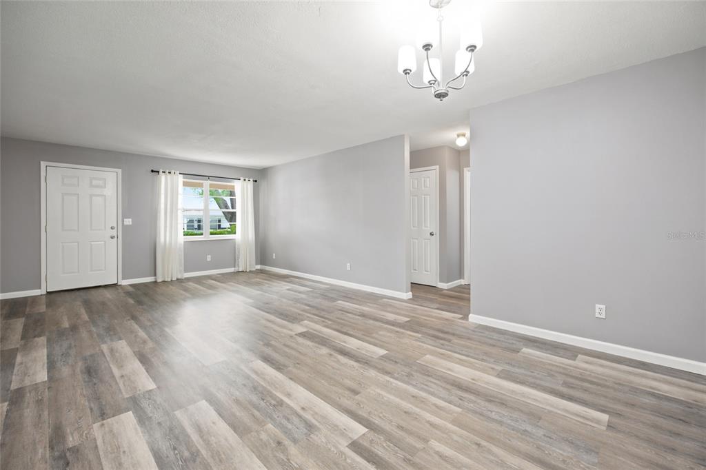 A living room with gray walls, wood-look flooring, a white front door, and a chandelier — 8710 SW 96TH STREET UNIT C, OCALA, FL