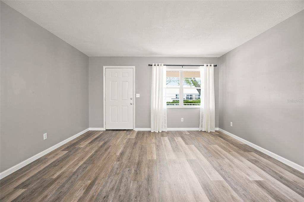 An empty room features gray walls, wood-look flooring, a white front door, and a window — 8710 SW 96TH STREET UNIT C, OCALA, FL