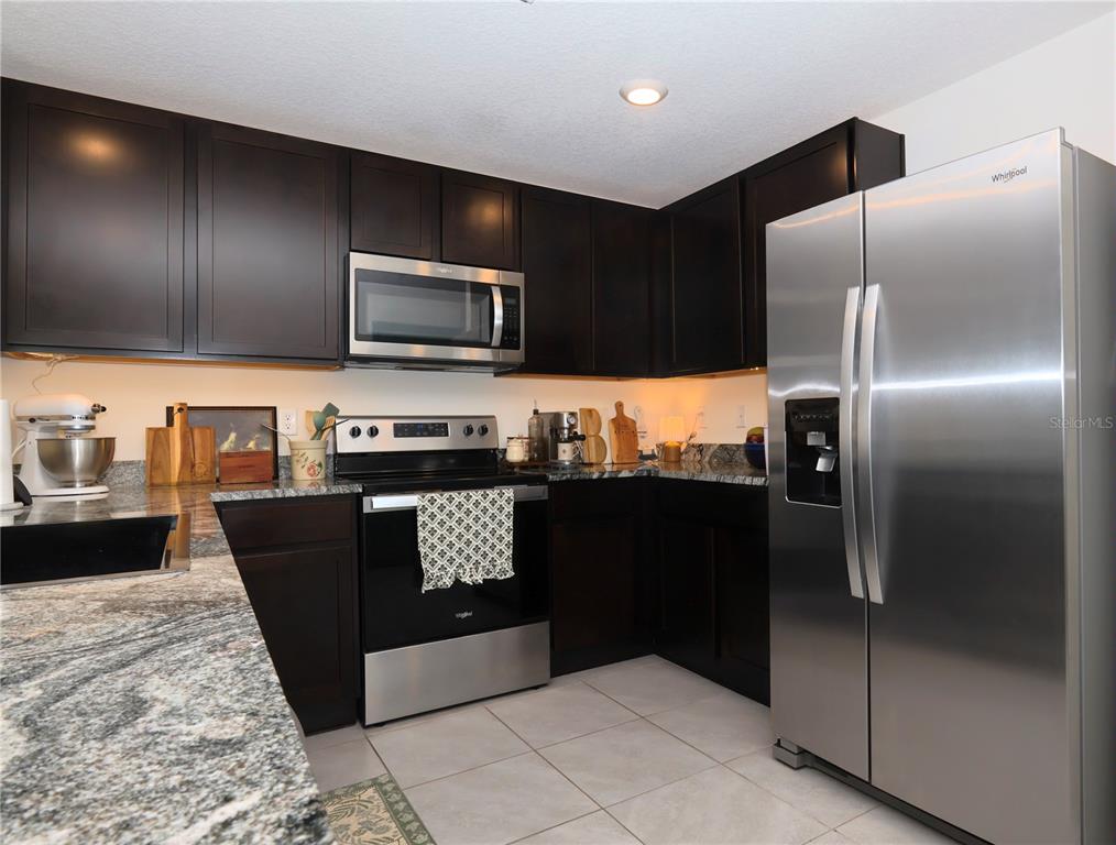 A kitchen featuring dark wood cabinets, granite countertops, and stainless steel appliances — 13726 WHISKEY DAISY DRIVE, DADE CITY, FL