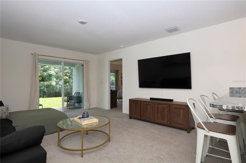 A living room with a wall-mounted television, a glass coffee table, and a sliding glass door — 13726 WHISKEY DAISY DRIVE, DADE CITY, FL