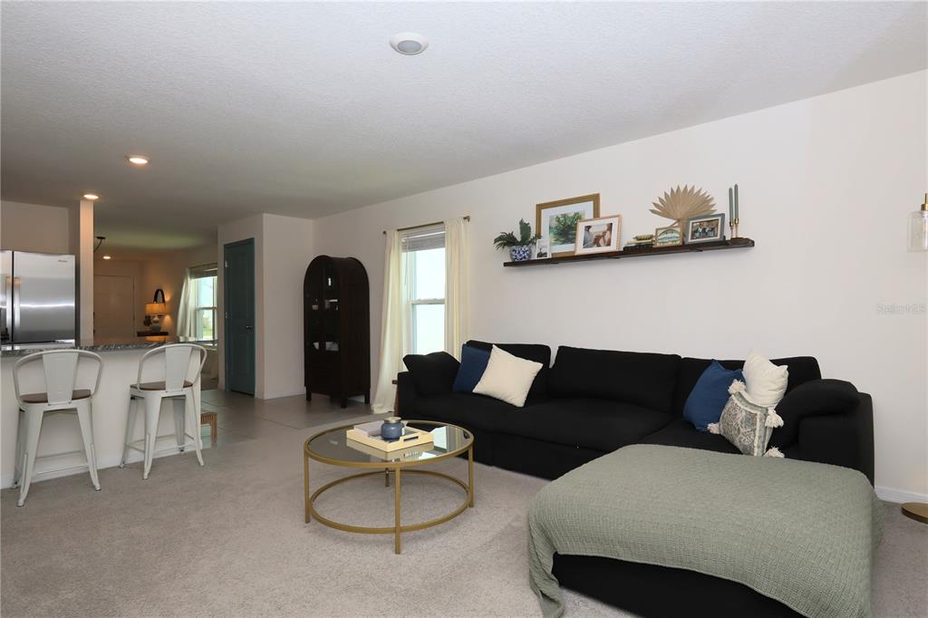 A living room features a black sectional sofa, a glass coffee table, and a wall shelf — 13726 WHISKEY DAISY DRIVE, DADE CITY, FL