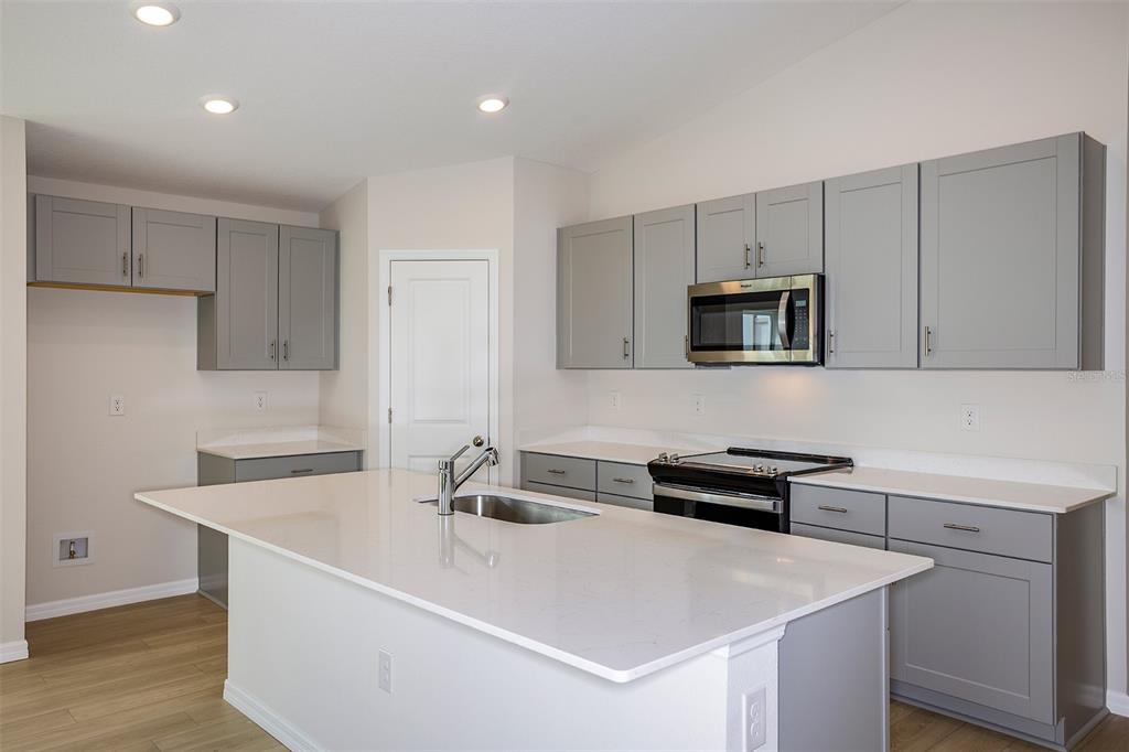 A kitchen features gray cabinets, white countertops, a central island with a sink, and stainless appliances — 36691 THORNHEDGE DRIVE, ZEPHYRHILLS, FL