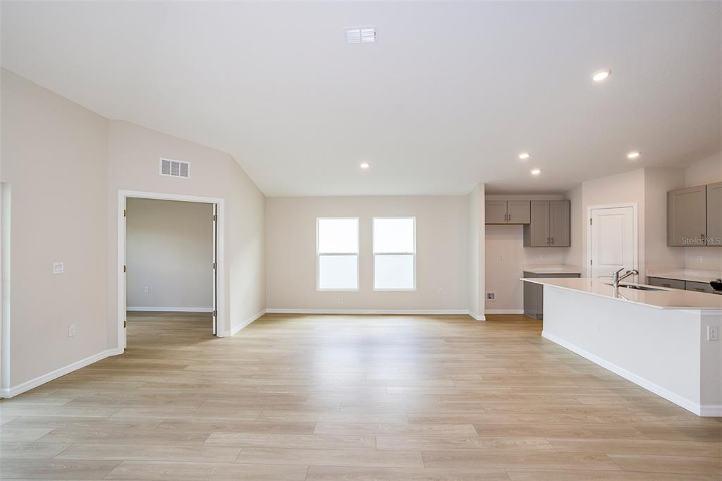 An open-concept living area features light wood-look flooring, a kitchen island, and neutral walls — 36691 THORNHEDGE DRIVE, ZEPHYRHILLS, FL