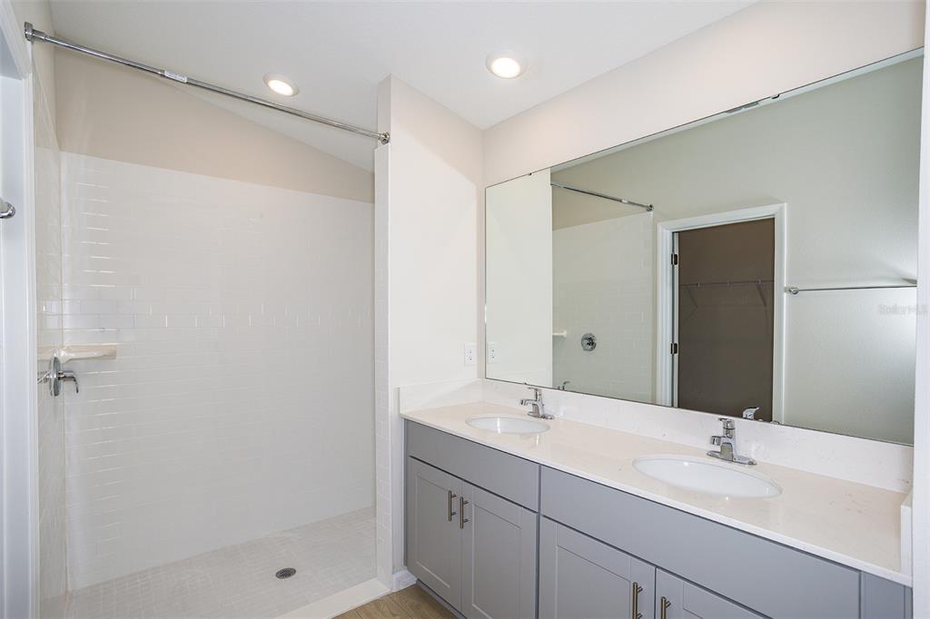 A bathroom features a walk-in shower with white tile and a gray double-sink vanity — 36691 THORNHEDGE DRIVE, ZEPHYRHILLS, FL
