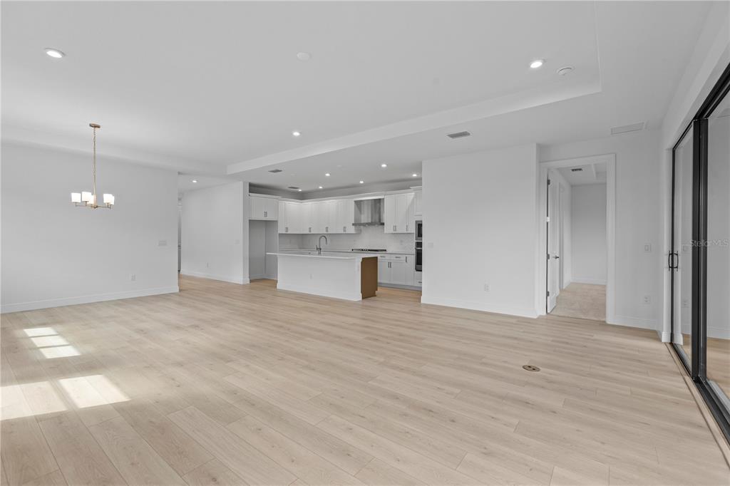 A modern kitchen with white cabinetry and an island opens to a spacious living area — 5032 LOWLAND TERRACE, PARRISH, FL