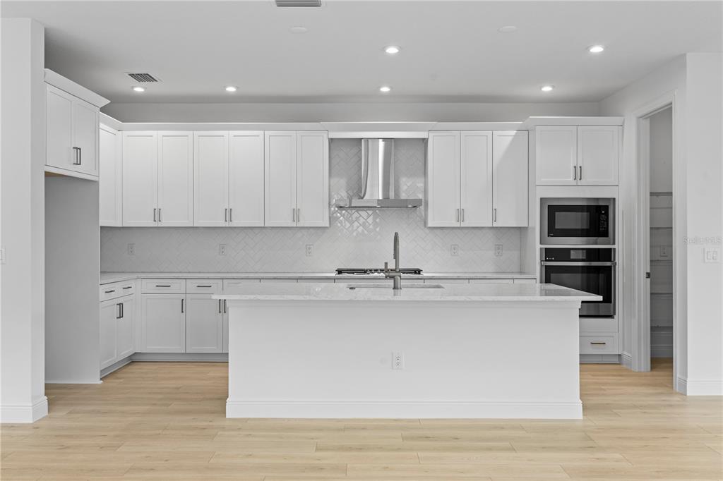 An open-concept kitchen and living area feature light wood flooring, white cabinetry, and recessed lighting — 5032 LOWLAND TERRACE, PARRISH, FL