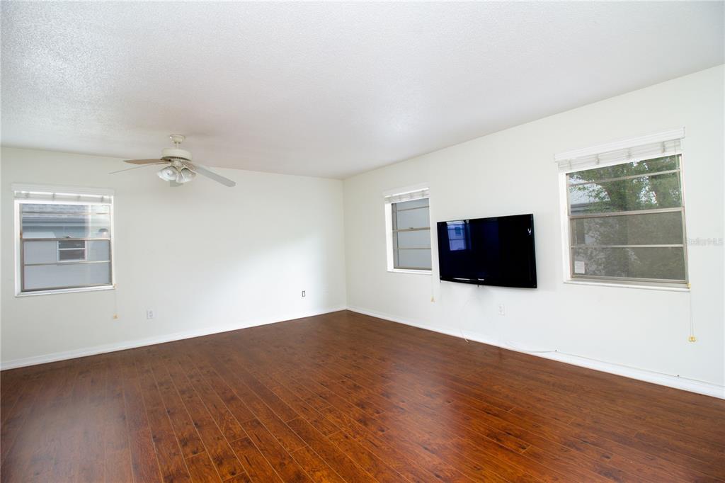 An empty living room with dark wood flooring, white walls, a ceiling fan, and a television — 6940 A SUNSET DRIVE S UNIT 2C, ST PETERSBURG, FL