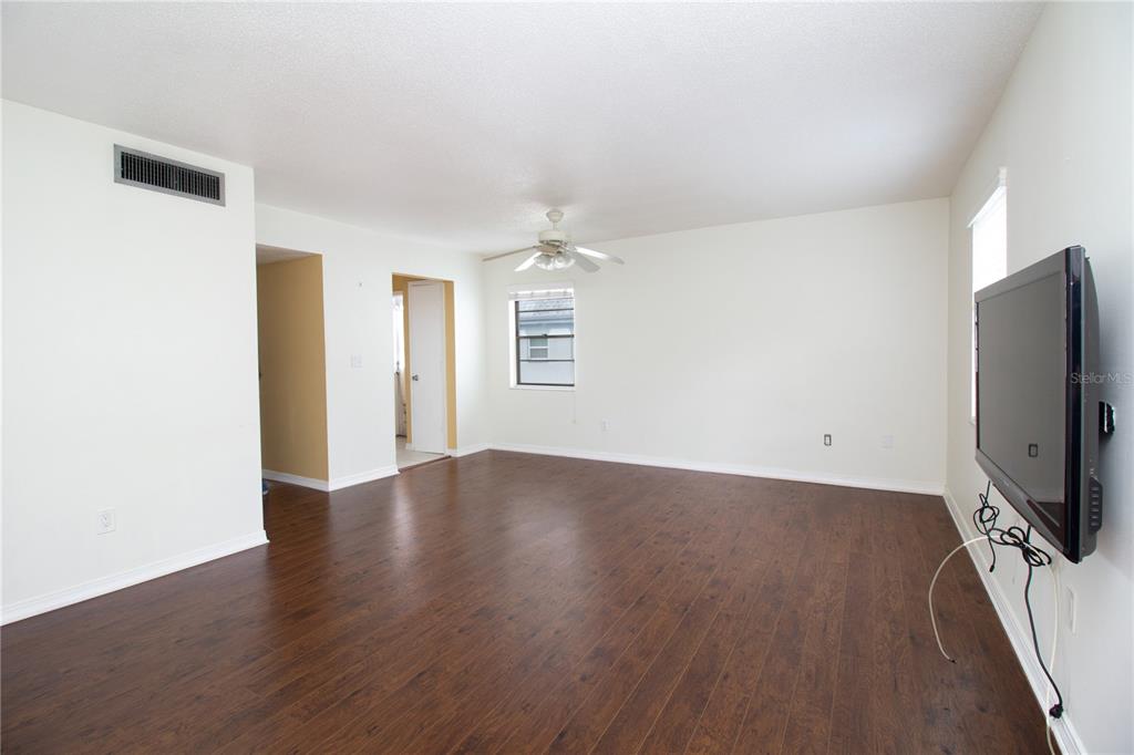 An empty living room features dark wood-look flooring, white walls, a ceiling fan, and television — 6940 A SUNSET DRIVE S UNIT 2C, ST PETERSBURG, FL