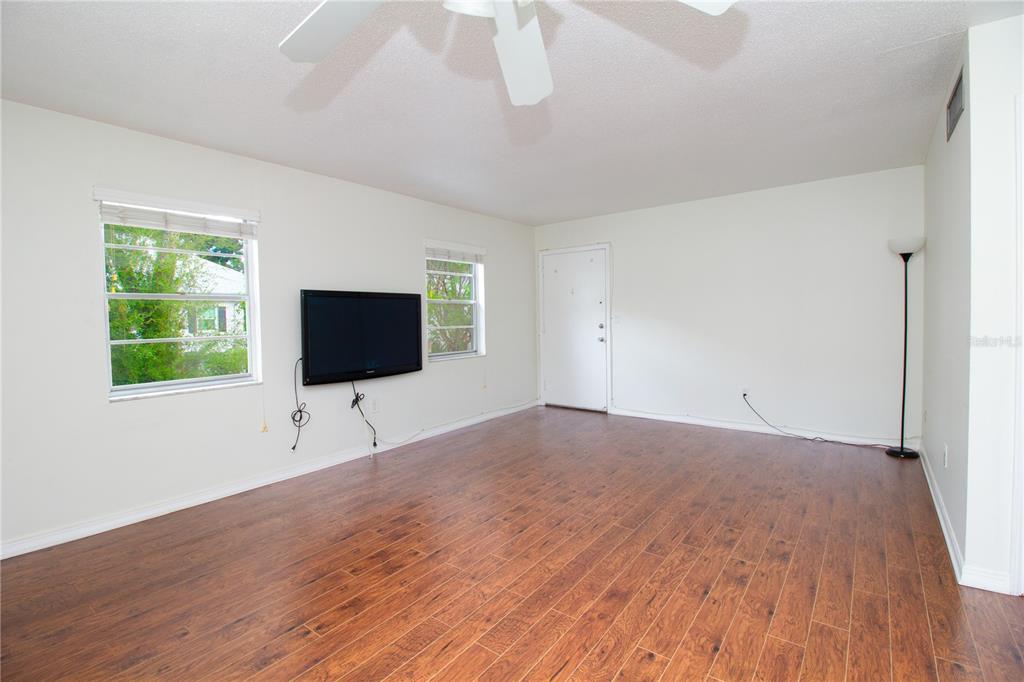 A living room with wood-look flooring, a wall-mounted television, and a white ceiling fan — 6940 A SUNSET DRIVE S UNIT 2C, ST PETERSBURG, FL