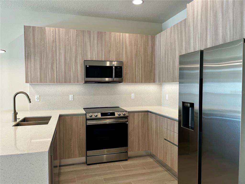 A modern kitchen features light wood cabinets, stainless steel appliances, and white quartz countertops — 1427 SERENDIPITY LANE, CLERMONT, FL