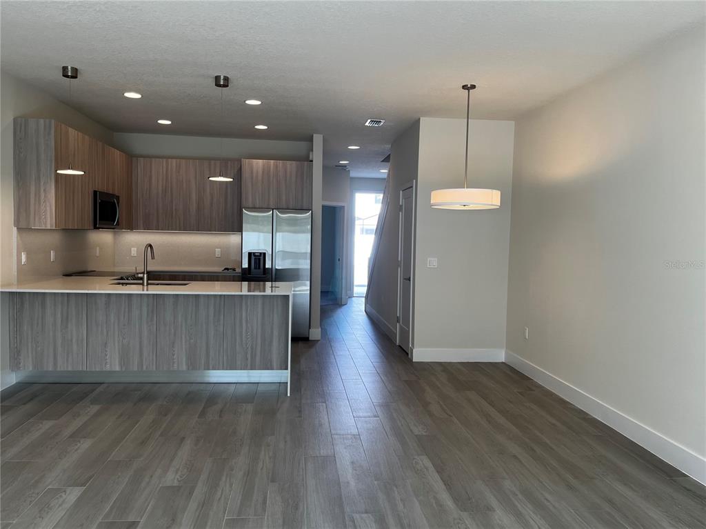 A modern kitchen with wood-grain cabinets and a breakfast bar overlooks an open living area — 1427 SERENDIPITY LANE, CLERMONT, FL