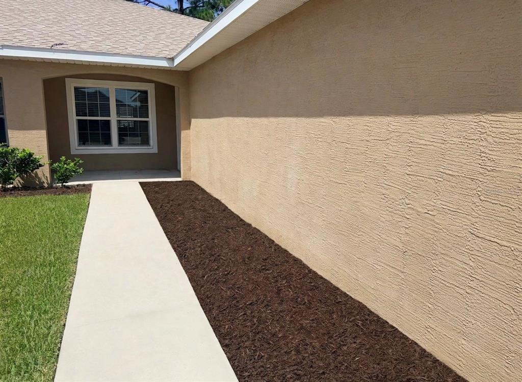 A beige stucco exterior wall runs alongside a concrete walkway and a bed of mulch — 20 RAINSTONE LANE UNIT B, PALM COAST, FL
