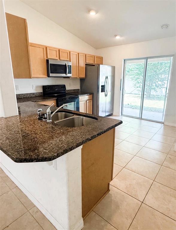 A kitchen features wood cabinets, granite countertops, stainless steel appliances, and tile flooring — 20 RAINSTONE LANE UNIT B, PALM COAST, FL