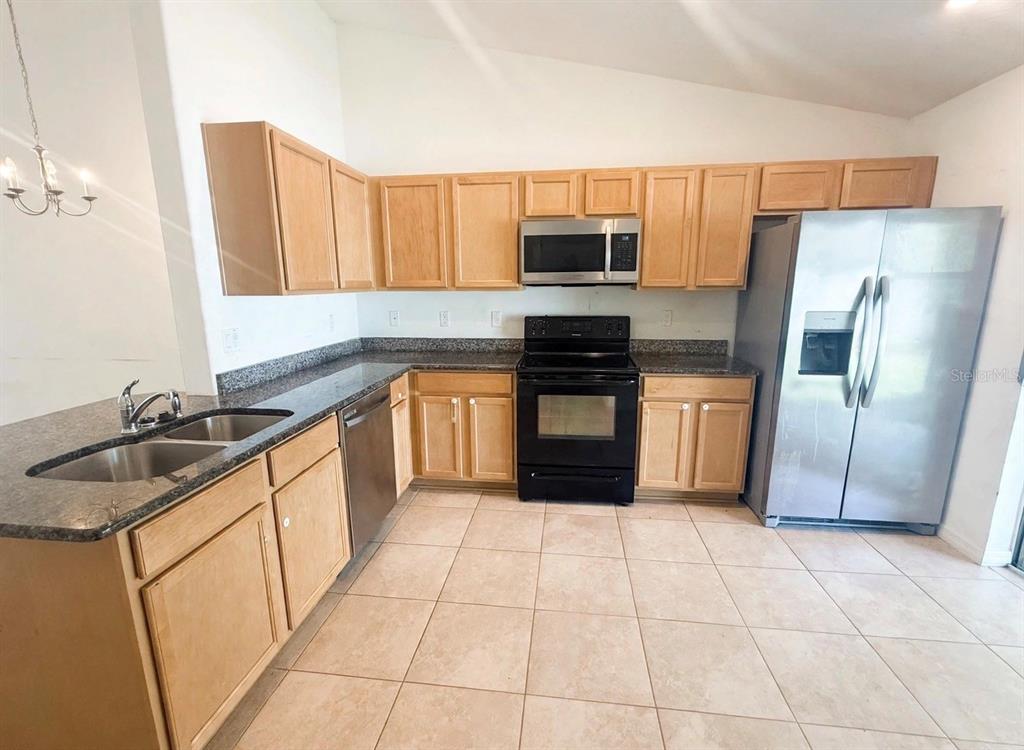 A kitchen features light wood cabinets, dark granite countertops, stainless steel appliances, and tile flooring — 20 RAINSTONE LANE UNIT B, PALM COAST, FL