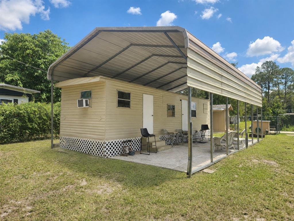 A tan mobile home sits under a large metal carport on a grassy lot — 23824 NE 188TH PLACE, FORT MC COY, FL
