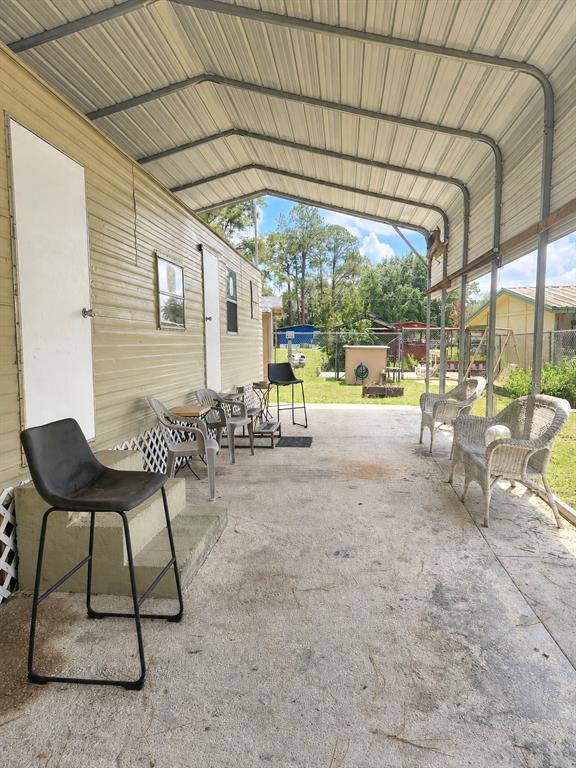 A concrete patio area features a metal carport cover and several outdoor chairs — 23824 NE 188TH PLACE, FORT MC COY, FL