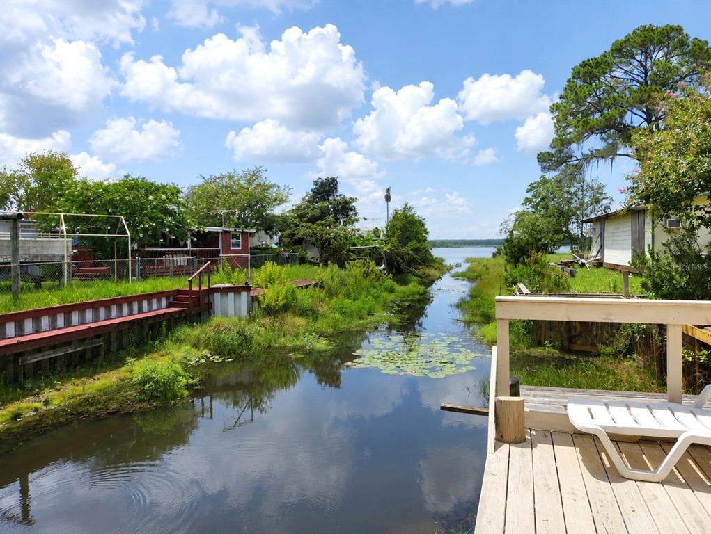 A wooden deck overlooks a narrow canal leading to a lake surrounded by trees and houses — 23824 NE 188TH PLACE, FORT MC COY, FL