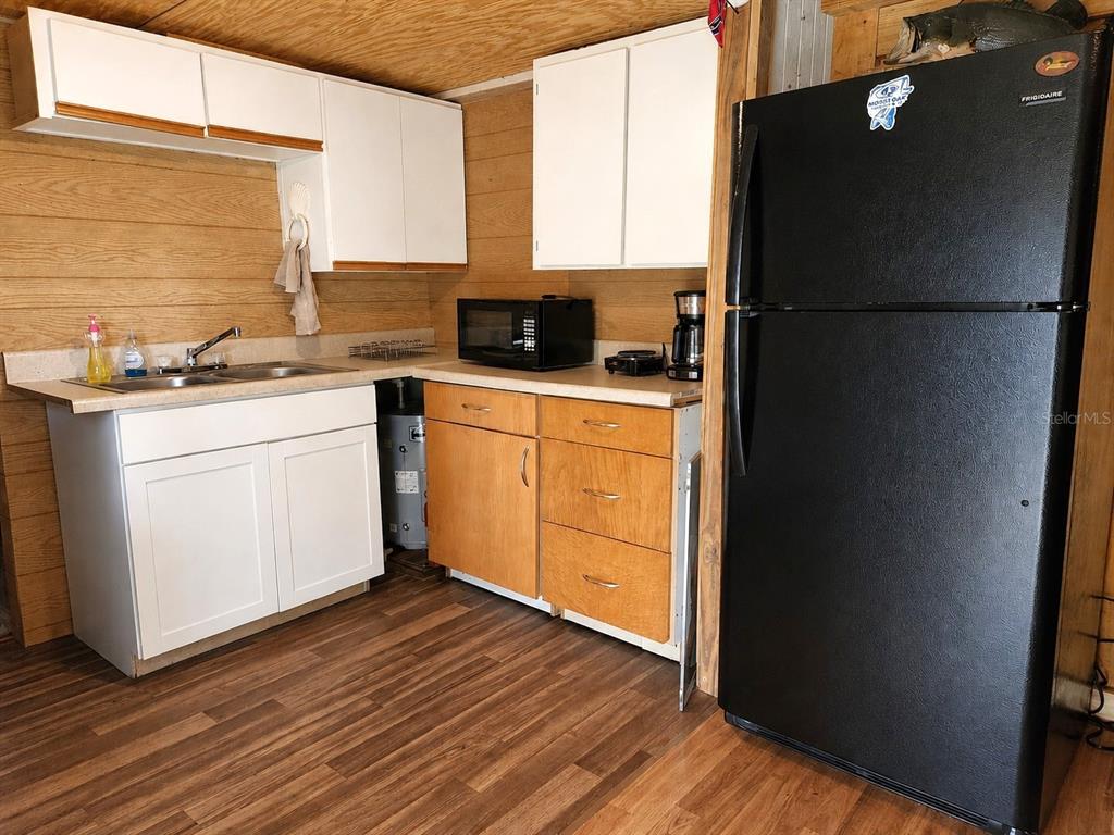 A kitchen features wood-paneled walls, white upper cabinets, wood lower cabinets, and a black refrigerator — 23824 NE 188TH PLACE, FORT MC COY, FL