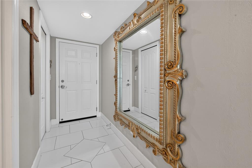 A white-tiled entryway features a large ornate gold-framed mirror and a wooden wall cross — 2937 S ATLANTIC AVENUE UNIT 2002, DAYTONA BEACH SHORES, FL