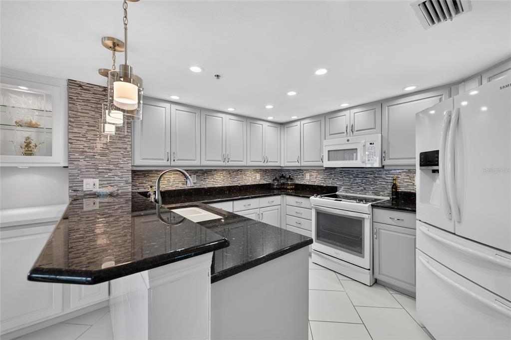 A kitchen features light gray cabinets, dark granite countertops, a tiled backsplash, and white appliances — 2937 S ATLANTIC AVENUE UNIT 2002, DAYTONA BEACH SHORES, FL