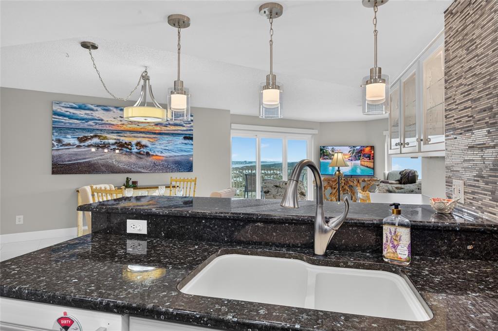 A kitchen features dark granite countertops, a white double-basin sink, and pendant lighting over the island — 2937 S ATLANTIC AVENUE UNIT 2002, DAYTONA BEACH SHORES, FL