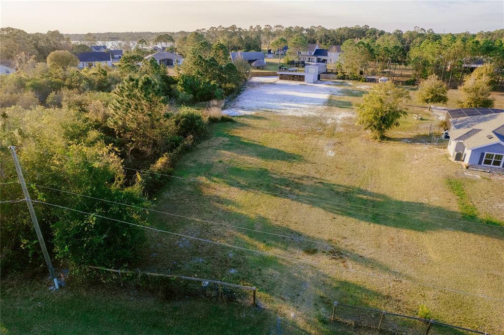 An aerial view shows a large, grassy residential lot with a shed and surrounding trees — 7011 BRIDLE PATH, ST CLOUD, FL