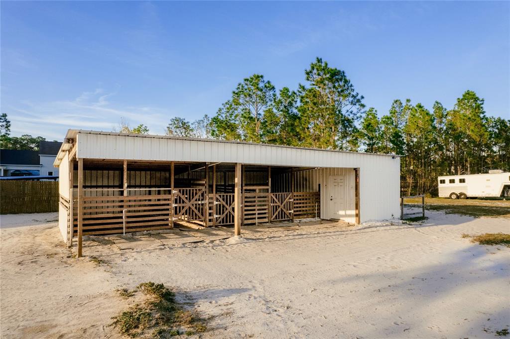 A white metal barn with multiple horse stalls stands on a sandy lot — 7011 BRIDLE PATH, ST CLOUD, FL