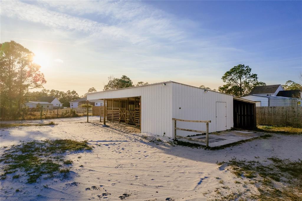 A white metal barn with open stalls sits on a sandy lot under a sunny sky — 7011 BRIDLE PATH, ST CLOUD, FL