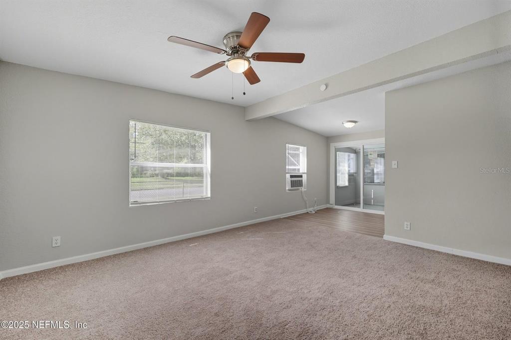 A carpeted living room features a ceiling fan, light gray walls, and a sliding glass door — 5306 PARIS AVENUE, JACKSONVILLE, FL