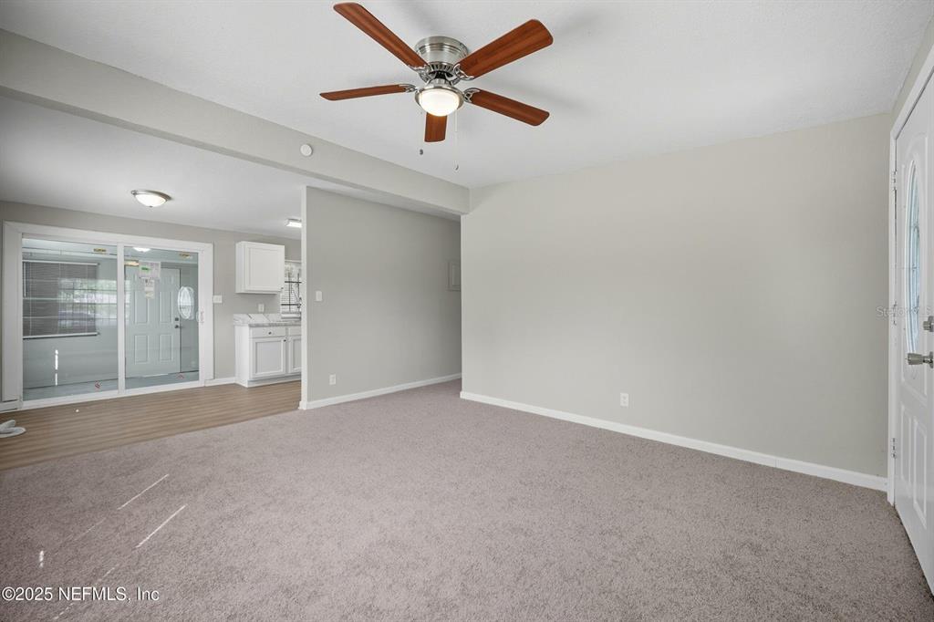 A carpeted living room features a ceiling fan and an adjacent kitchen with white cabinets — 5306 PARIS AVENUE, JACKSONVILLE, FL