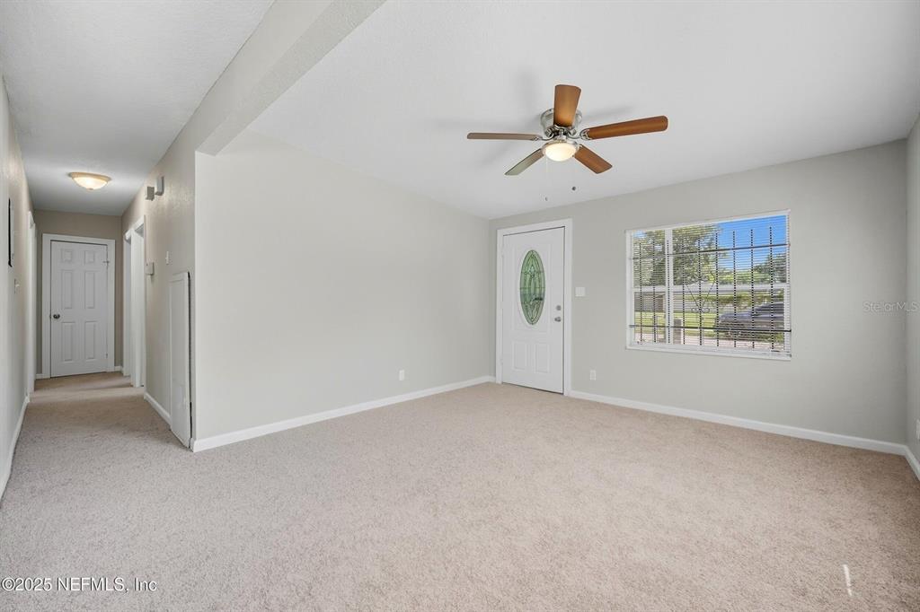 A carpeted living room features a ceiling fan, a front door, and a window — 5306 PARIS AVENUE, JACKSONVILLE, FL